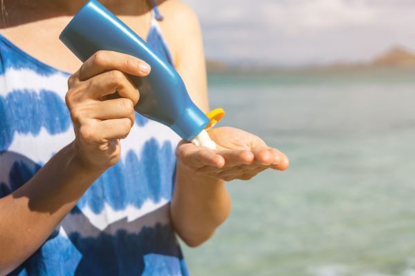 Mulher na beira da praia colocando protetor solar na mão