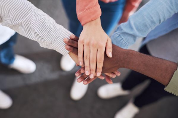 O trabalho em equipe sendo representado pelo entrelaçamento de mãos masculinas e femininas de raças diferentes.