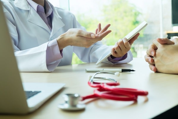 Médica realizando anamnese com paciente no consultório. Imagem demonstra o conceito de colaboração do paciente durante a consulta.